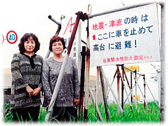 佐賀関女性防火防災クラブが設置した避難呼び掛け看板。同クラブ瀧川会長(左)、会員の西田さん